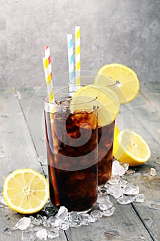 Softdrink with ice cubes, lemon and straw in glass.