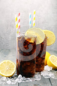 Softdrink with ice cubes, lemon and straw in glass.