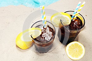 Softdrink with ice cubes, lemon and straw in glass.