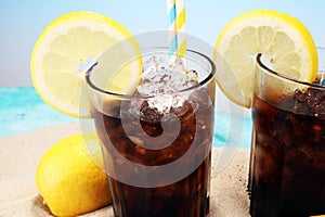 Softdrink with ice cubes, lemon and straw in glass.