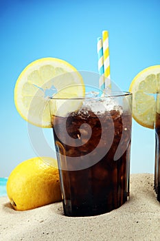 Softdrink with ice cubes, lemon and straw in glass.