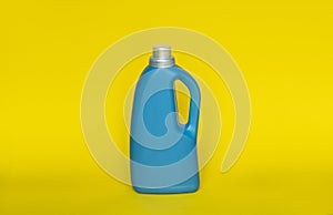 Softener in blue plastic bottle isolated on yellow background. Bottle with liquid laundry detergent, cleaning agent