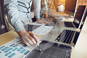 Software developer is pointing to the paper working and analyzing together the code written into the program on the computer