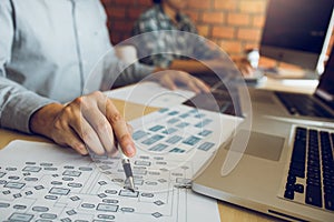 Software developer is pointing to the paper working and analyzing together the code written into the program on the computer