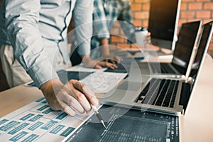 Software developer is pointing to the paper working and analyzing together the code written into the program on the computer