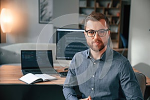 Software developer is sitting and posing. Man in formal clothes is working in the modern office. Using computer