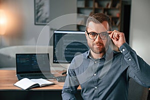 Software developer is sitting and posing. Man in formal clothes is working in the modern office. Using computer