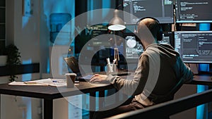 Software engineer typing programming code on laptop with multiple monitors