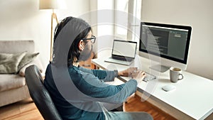 Software Programming. Side view of young male web developer wearing eyeglasses writing code on desktop computer, working photo