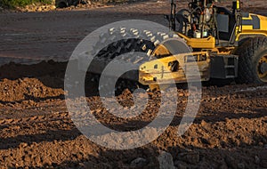 Soil compactor with vibratory padfoot drum. Heavy duty machinery working on highway construction site. Vehicle for soil