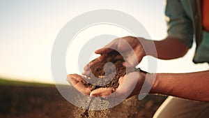 Soil in the hands of the farmer. Sun agriculture. Close-up of a farmers hands holding black soil in their hands, fertile