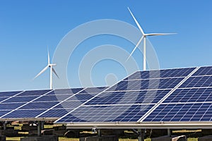 Solar cells with wind turbines generating electricity in hybrid power plant systems station on blue sky background