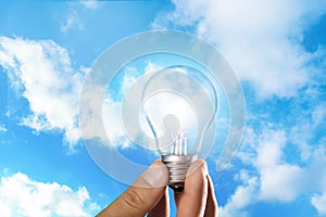 Solar energy concept. Man holding glowing light bulb against blue sky with clouds