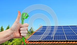 Solar energy panel on the roof of the house and hand holding green electric plug in sunny day.