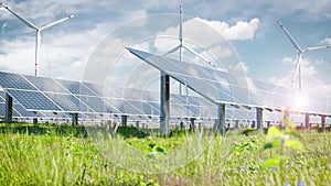 Solar farm of photovoltaic panels on a beautiful green meadow with wind turbines in the background