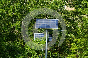 Solar panel on the background of green trees. On a pole on the street. Production of renewable energy concept.