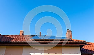 Solar panel on the red house roof in the background of blue sky.