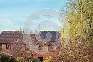 Solar panel on a red roof house, trees and blue sky. Alternative green energy concept. Selective focus, copy space