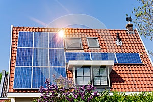 Solar panel on a red roof reflecting the sun and the cloudless blue sky