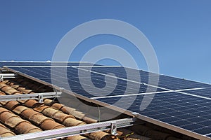 Solar panel on a red roof reflecting the sun and the cloudy blue sky in background