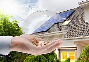 Solar panel on roof of house and coins in hand. Concept of money saving and clean energy photo
