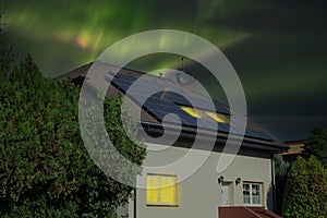 Solar Panel on the roof with the Northern Lights or Aurora borealis in the sky. Dawn in the windows