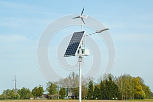 The solar panel stands on a pole with a street lamp against the blue sky.