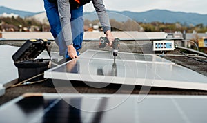 Solar panel technician with drill installing solar panels on roof on family house a sunny day