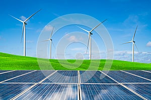 Solar panel and wind turbines farm on green hills.