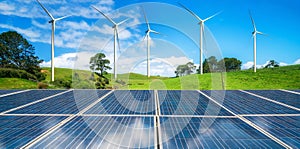 Solar panel and wind turbines farm on green hills.