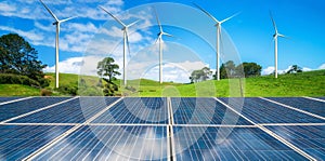 Solar panel and wind turbines farm on green hills