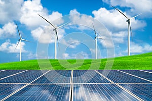 Solar panel and wind turbines farm on green hills.