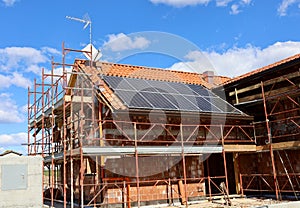 Solar panels already installed on the roof of a house under construction covered with scaffolding