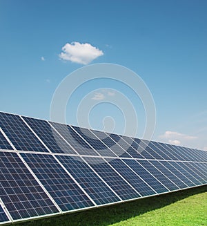 Solar panels of a battery of photocells against a background of clouds and a blue sky green grass