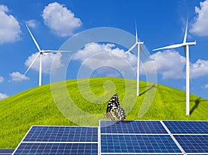 Solar panels and butterfly with wind turbines on grass hill and blue sky
