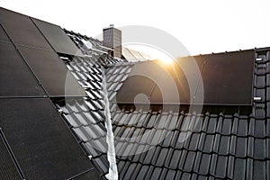 Solar panels on a dark tiled roof captured with a lens flare at sunrise