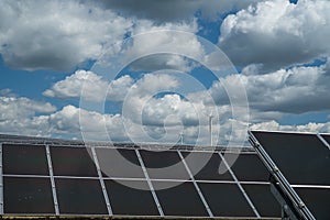 Solar panels in the field under the cloudy sky with windmill turbines in the background