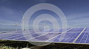 Solar panels with wind turbines against blue sky background.