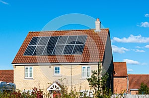 Solar photovoltaic panel array on house roof against a blue sky