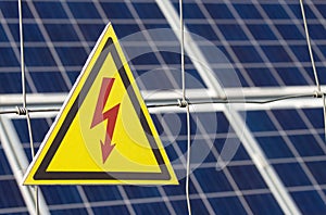 Solar power farm station on a background selective focus on a yellow triangular high voltage warning sign. The concept of