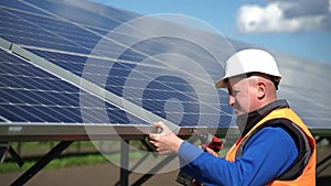 Solar power plant engineer fixing panels to metal base with bolts using a drill. Man with electric wrench repairing solar panels.