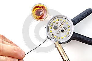 Soldering a burned-out LED into an LED light bulb. Hand with a soldering iron and rosin with solder on a white