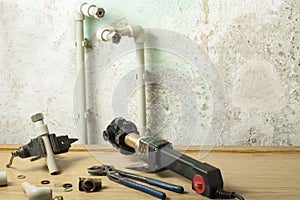 Soldering iron for plastic pipes and equipment for plumbing on wooden table on old wall background. Repairment concept.