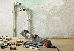 Soldering iron for plastic pipes and equipment for plumbing on wooden table on old wall background. Repairment concept.