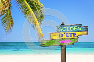 Soldes d`ete meaning summer sale in French written on pastel colored wood direction signs, beach and palm tree background