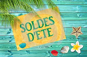 Soldes d`ete meaning summer sale in French written on yellow sign, blue wood planks, seashells, beach and palm tree backgroun photo