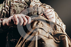 Soldier in camouflage jacket holding and unzipping tactical backpack