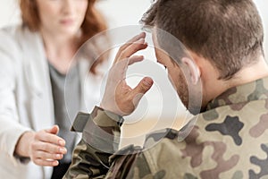 Soldier with headache wearing green moro uniform during meeting with psychotherapist photo