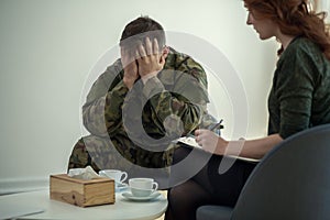 Soldier hiding his face in his hands while talking to a psychiatrist during therapy