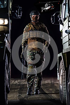 A soldier marching through the dark of night, accompanied by two military trucks, as he embarks on a perilous military